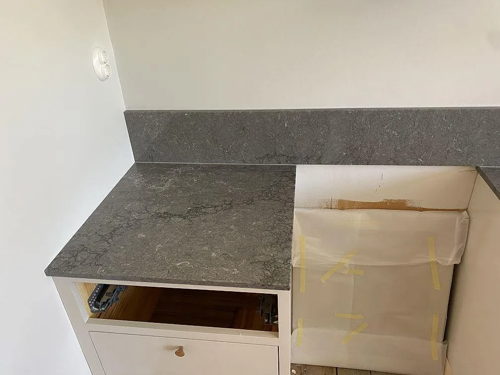 Detalj av köksbänkskiva och stänkskydd i Caesarstone Turbine Grey, grå kvartskomposit med rörelse i ytan, monterad över köksstommarna i ett kök i Göteborg.