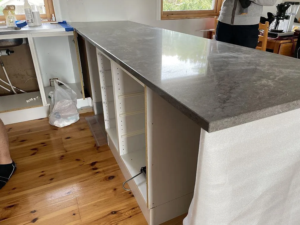 Lång polerad köksbänkskiva i Caesarstone Turbine Grey, grå komposit, monterad på vita köksstommar i Grundsund.