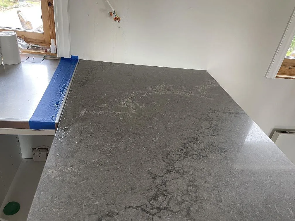 Ytbild av polerad Caesarstone Turbine Grey med grå ådring på köksbänkskiva vid fönster i Grundsund.