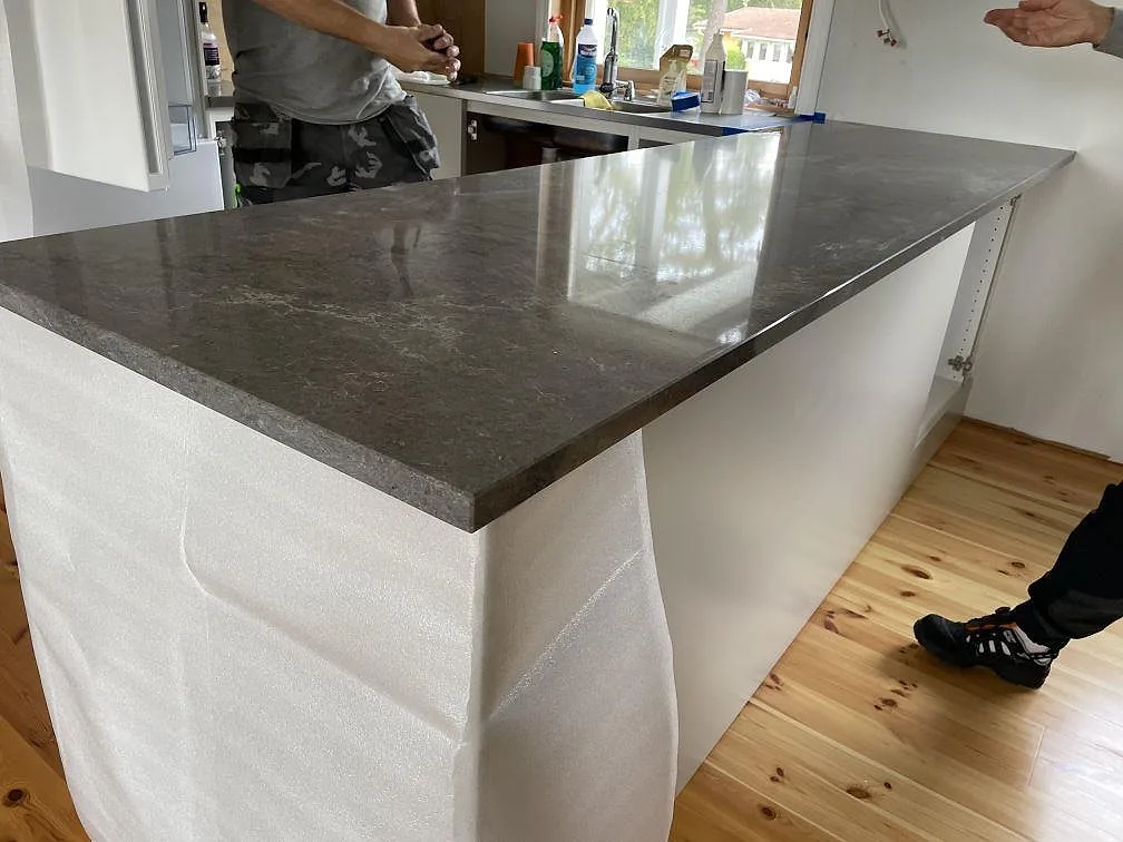 Närbild på polerad Caesarstone Turbine Grey som köksbänkskiva på vit halvö med trägolv i Grundsund.