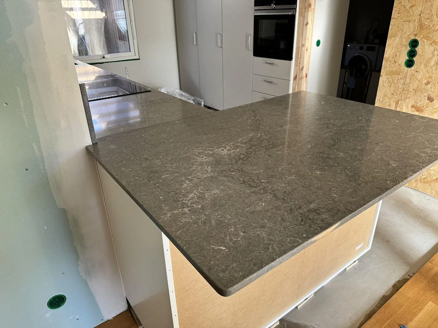 Köksö i Caesarstone Turbine Grey med polerad grå komposityta, fotograferad under montering i ett kök med vita stommar i Halmstad.