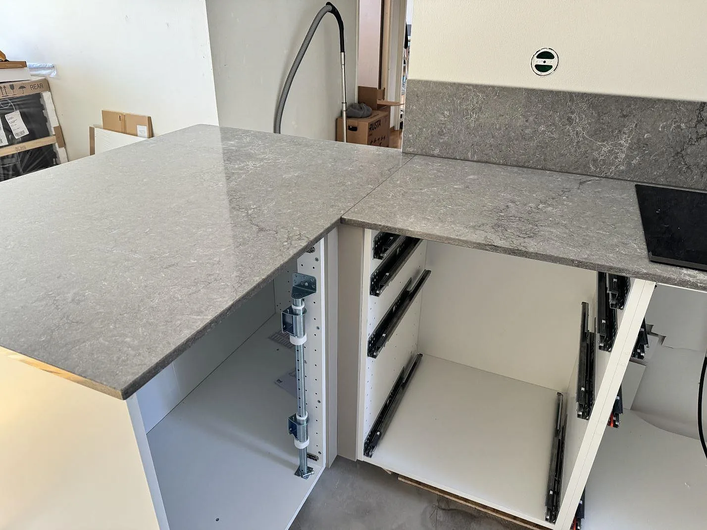 Köksö och väggbänk i Caesarstone Turbine Grey, polerad grå kvartskomposit, med öppna köksstommar under montering i Halmstad.