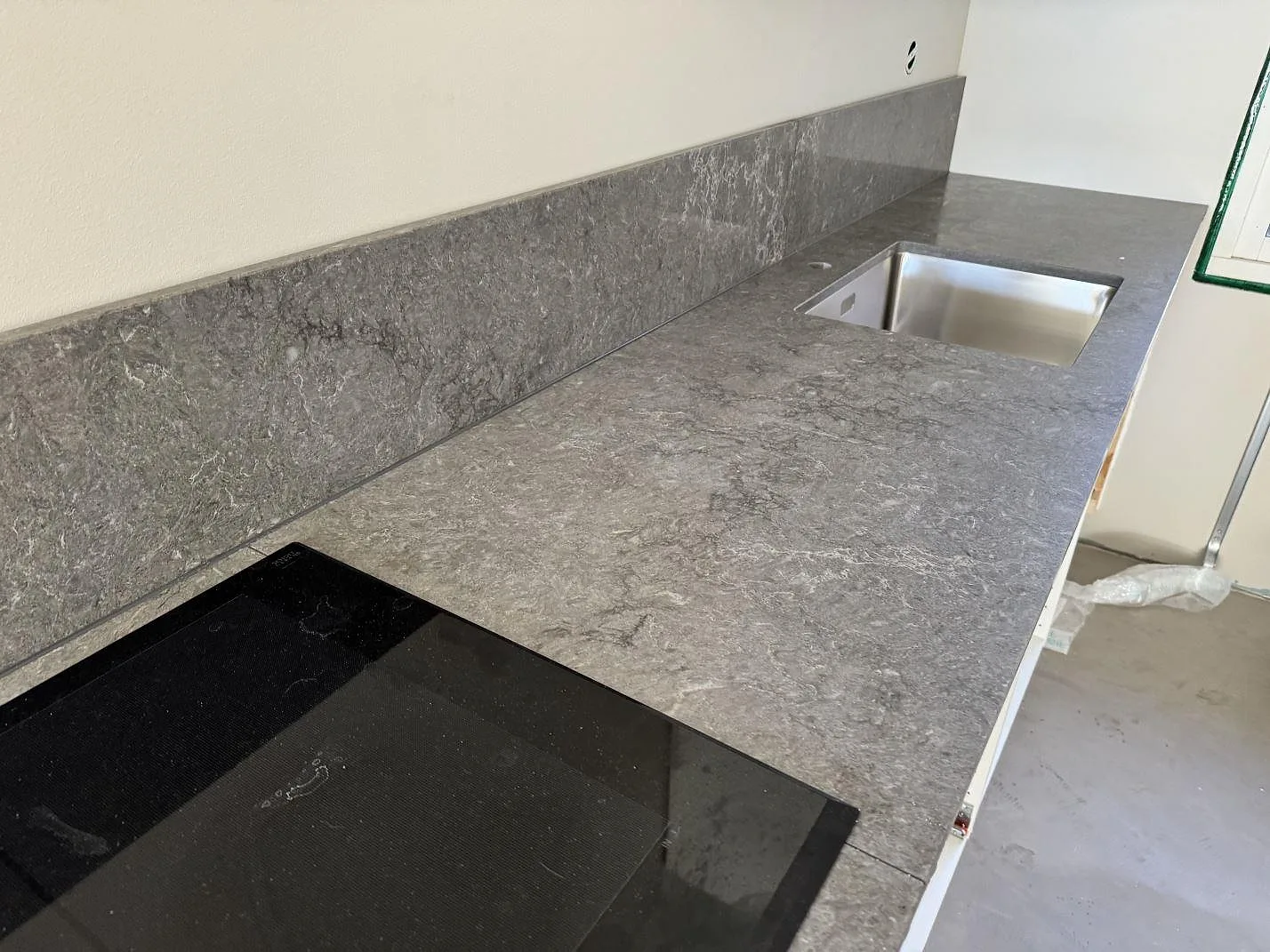 Lång köksbänkskiva i Caesarstone Turbine Grey, polerad grå kvartskomposit, med svart häll, underlimmad rostfri diskho och stänkkant i Halmstad.