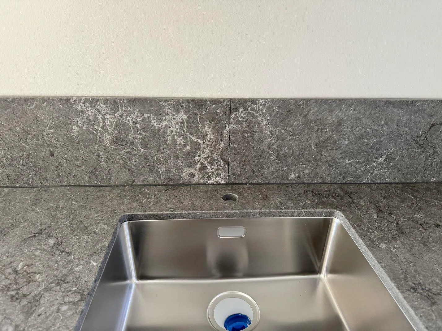 Detalj av underlimmad diskho och stänkkant i Caesarstone Turbine Grey, polerad grå komposit, monterad i Halmstad.