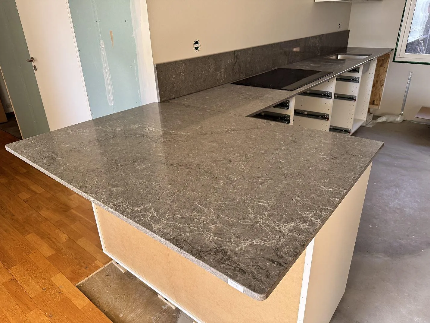 Köksbänkskiva i polerad Caesarstone Turbine Grey, grå kvartskomposit, med köksö, svart häll och väggbänk i ett kök i Halmstad.