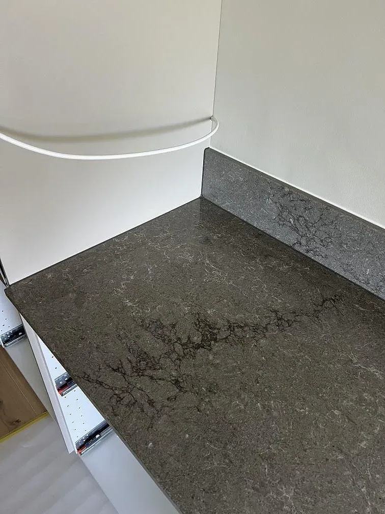 Närbild på polerad Caesarstone Turbine Grey, grå kompositbänkskiva med uppvikt kant vid vit vägg i Helsingborg.