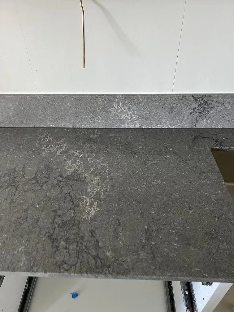 Detalj av polerad Caesarstone Turbine Grey som köksbänkskiva med uppvikt kant och grå marmorerad yta i Helsingborg.