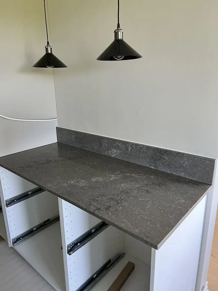 Polerad köksbänkskiva i Caesarstone Turbine Grey med uppvikt kant och vita skåpsstommar under montering i Helsingborg.