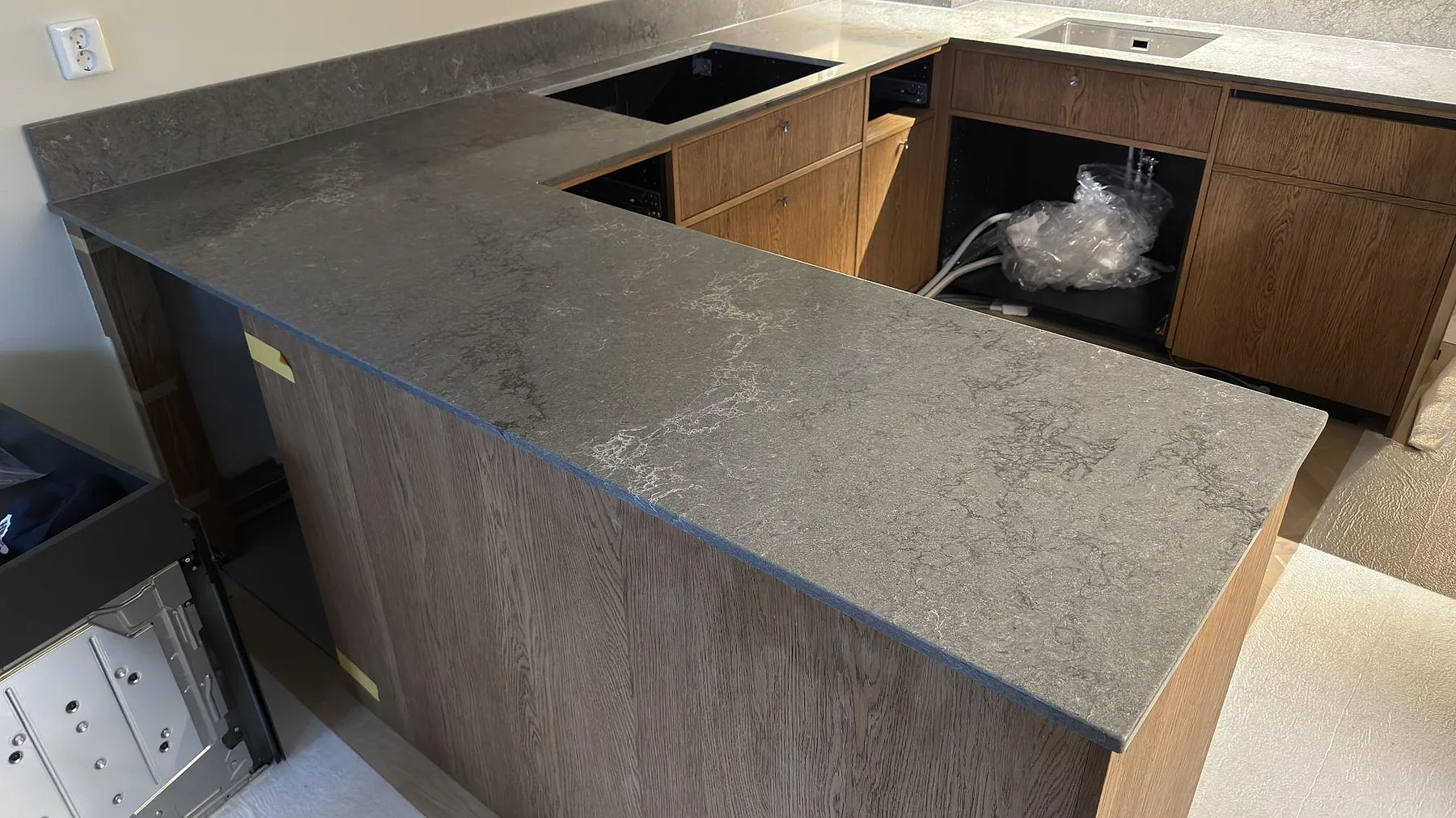 Köksbänkskiva i grå Caesarstone Turbine Grey, betongliknande kvartskomposit, sedd över halvön där den molniga ytstrukturen och den nedfällda kanten framträder, i ett kök i Sköndal.