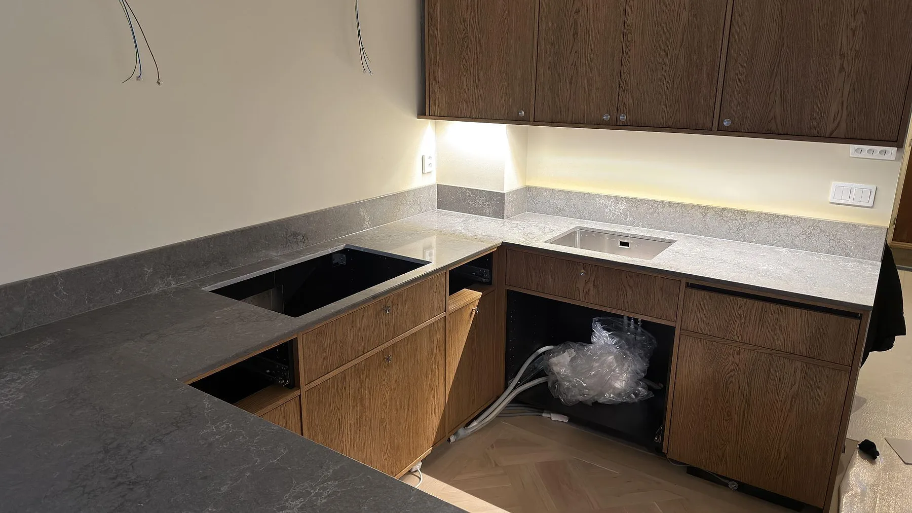 Vinklad köksbänk i grå Caesarstone Turbine Grey med underlimmad rostfri diskho och förberett hällurtag i den bakre raden, fotad under montering i ett kök i Sköndal.