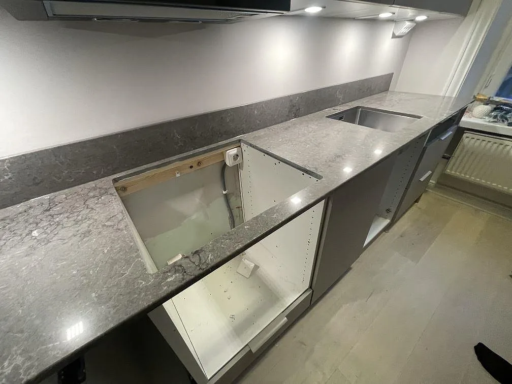 Köksbänkskiva i Caesarstone Turbine Grey med förberedd hällurtagning och fläktkåpa ovanför i ett kök i Stockholm.