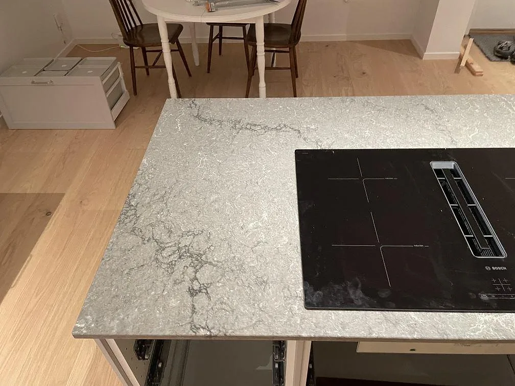 Polerad kompositbänkskiva i Caesarstone Turbine Grey bredvid svart häll och ljusa golv i Västra Frölunda.