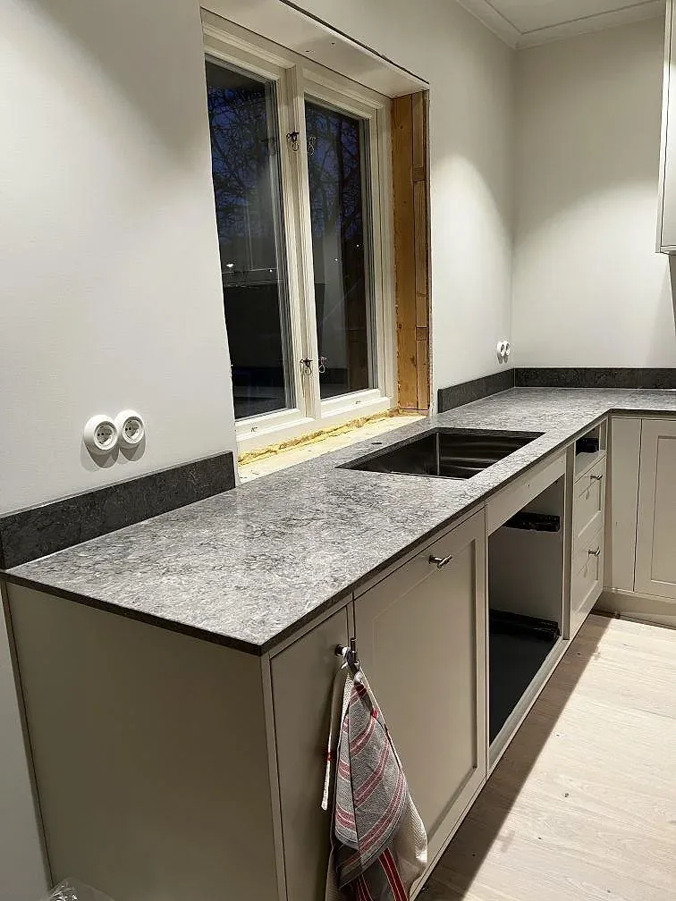Polerad köksbänkskiva i Caesarstone Turbine Grey med stänkskydd och fönsterbänk i samma grå sten i ett kök i Västra Frölunda.