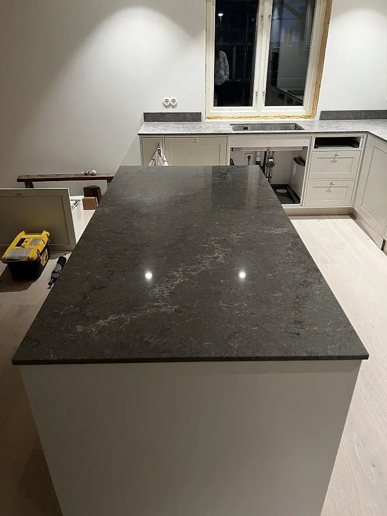 Köksö med polerad gråkoltonad Caesarstone Turbine Grey som speglar takspottar i ett kök i Västra Frölunda.