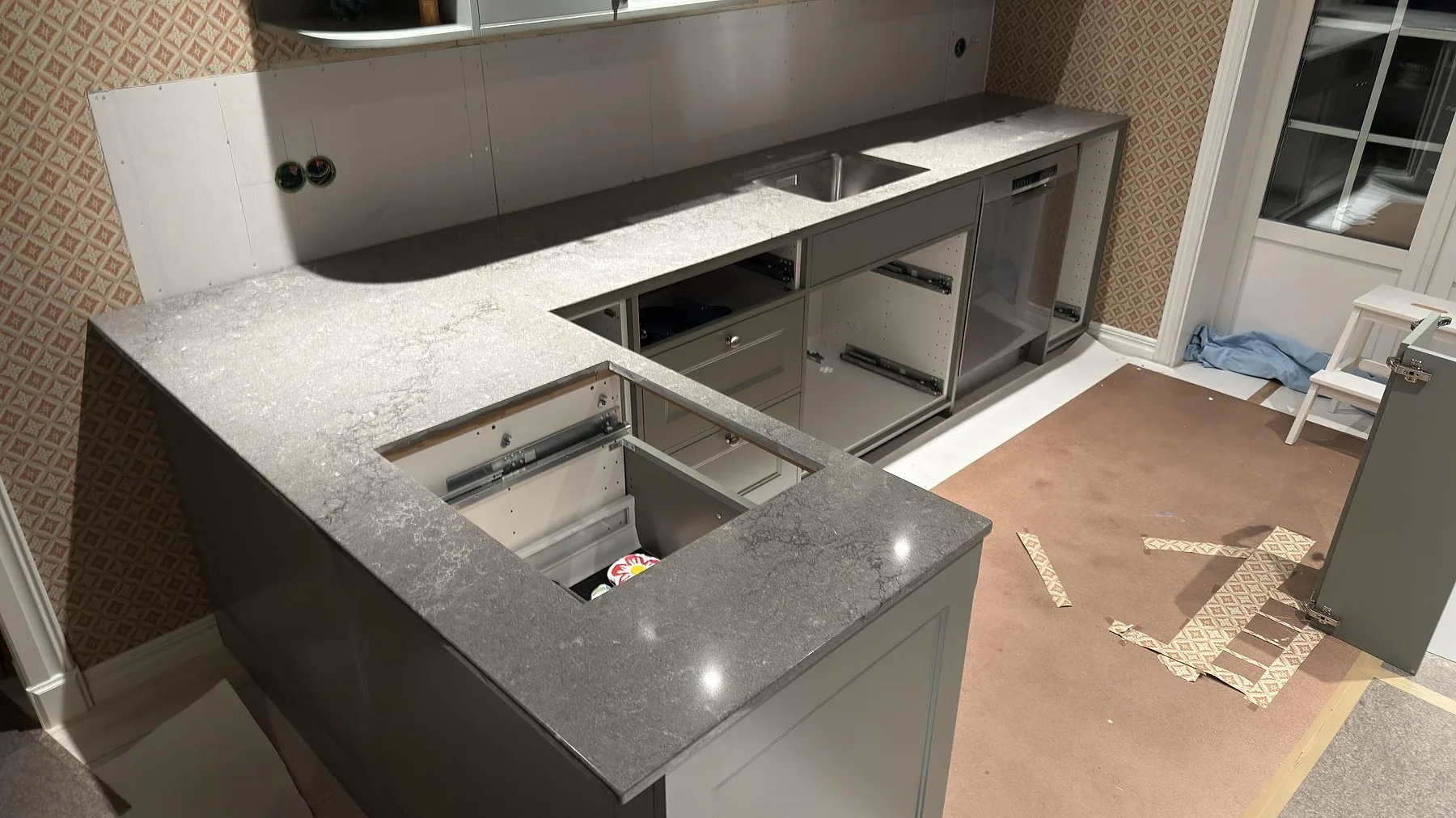 Köksbänkskiva i grå Caesarstone Turbine Grey, polerad komposit, monterad som vinklad bänk med köksö i ett kök under montering i Vallentuna.