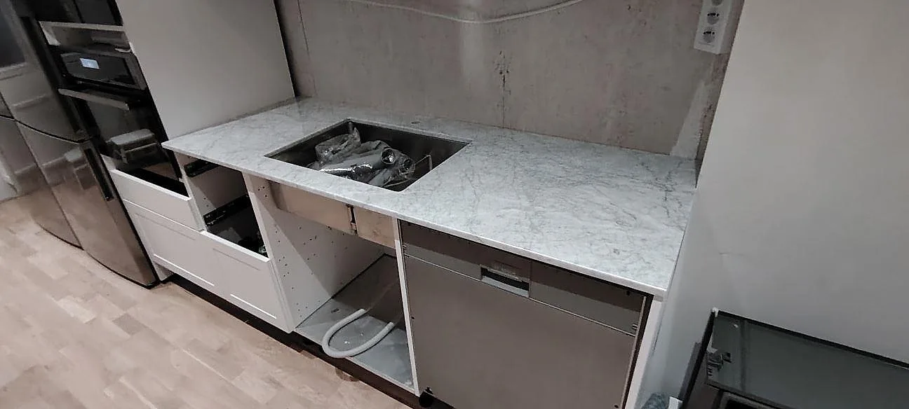 Rak köksbänkskiva i polerad Carrara C marmor, 20 mm, vid arbetsytan längs väggen i ett kök under montering i Åkersberga.