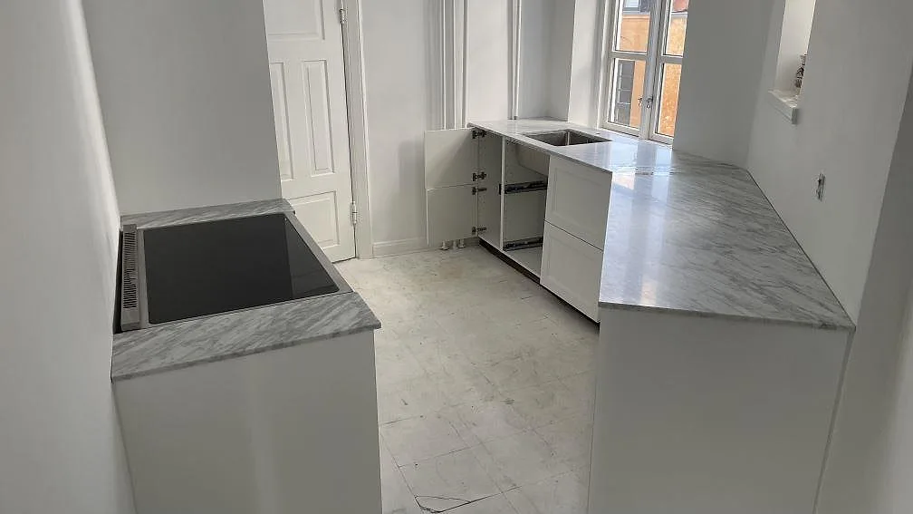 Köksbänkskiva i Carrara C marmor, matt 20 mm, i ett smalt vitt kök med spis och diskho i Aarhus C.