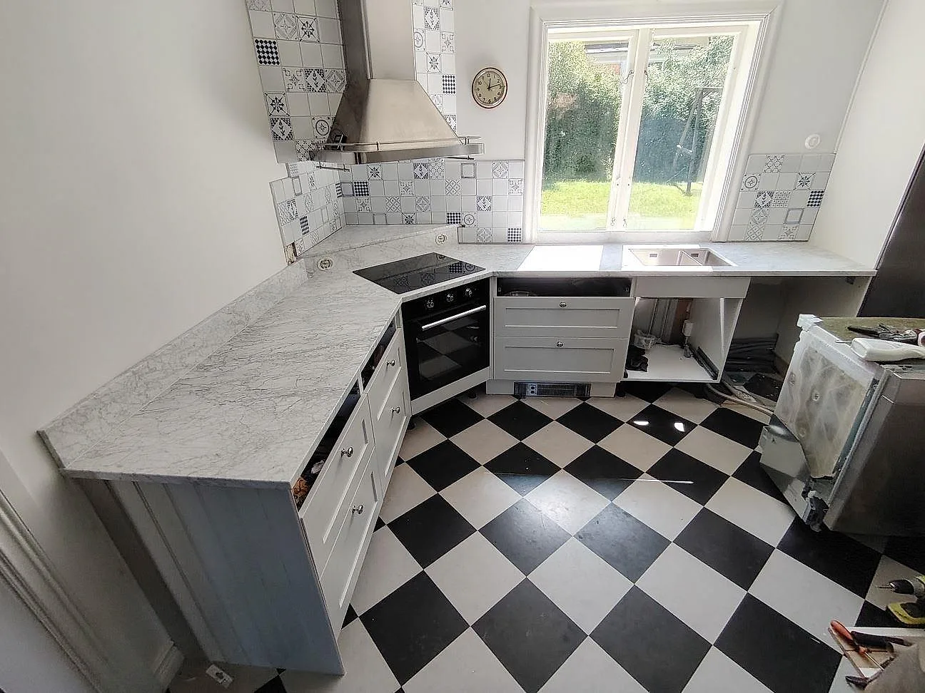 Köksbänkskiva i matt Carrara C marmor med häll, dubbel underlimmad rostfri diskho och svartvitt rutgolv i Älvsjö.