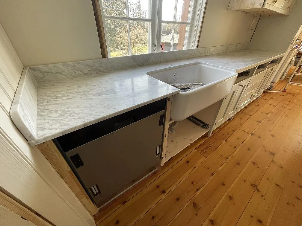 Köksbänkskiva i Carrara C marmor, matt 20 mm, med låg stänkkant och vit frontdiskho i ett kök i Älvsjö.