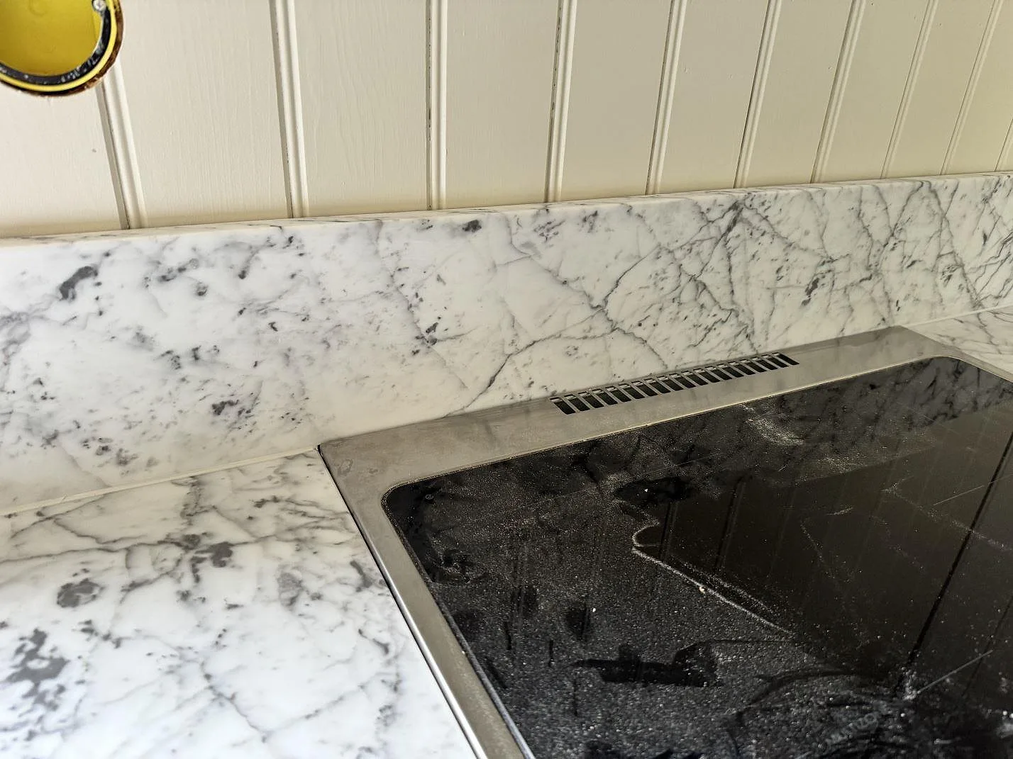Detalj av infälld häll i en matt Carrara C köksbänkskiva med uppvikt marmorstänkkant i Alstermo.
