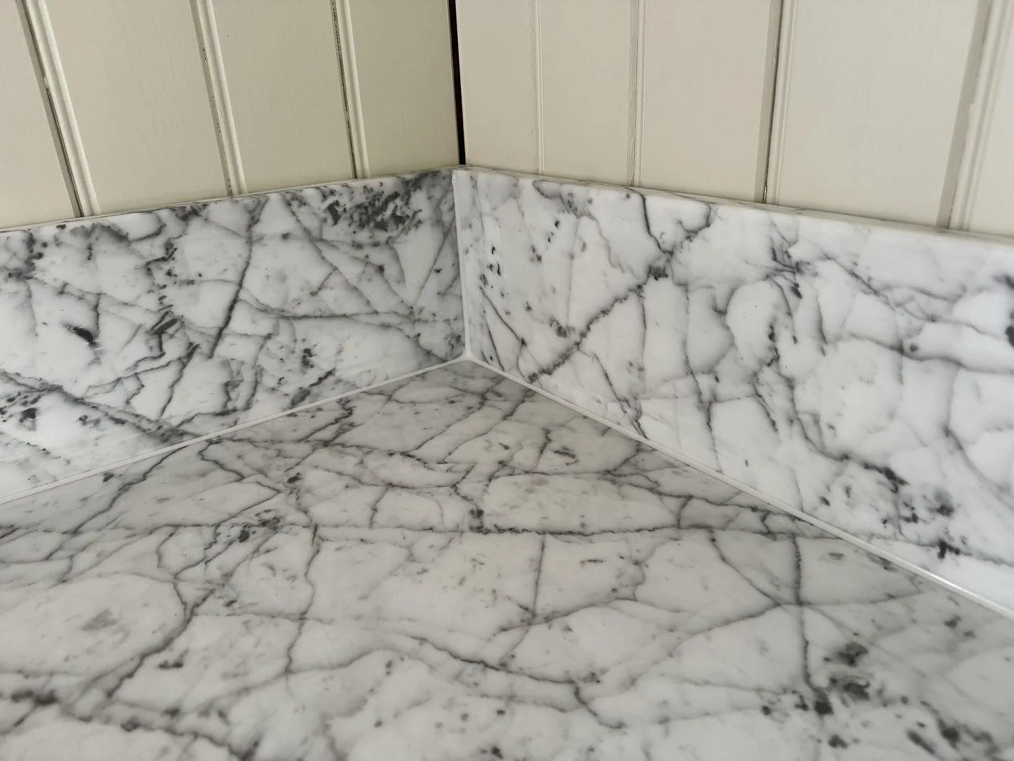 Närbild på matt Carrara C marmor med låg stänkkant och kraftig grå ådring mot vit pärlspont i köket i Alstermo.