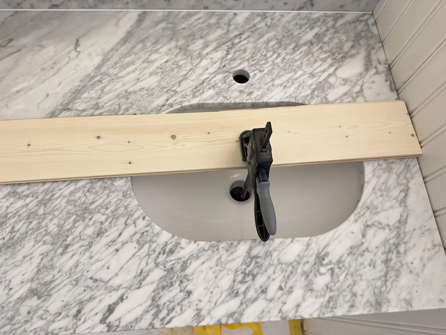 Bänkskiva i vit Carrara C marmor, matt, med underlimmat keramiktvättställ och borrat blandarhål samt kraftig grå ådring i ett badrum i Alstermo.