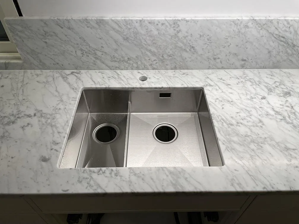 Underlimmad rostfri dubbelho i en köksbänkskiva av matt Carrara C-marmor med matchande stänkskydd i Avesta.