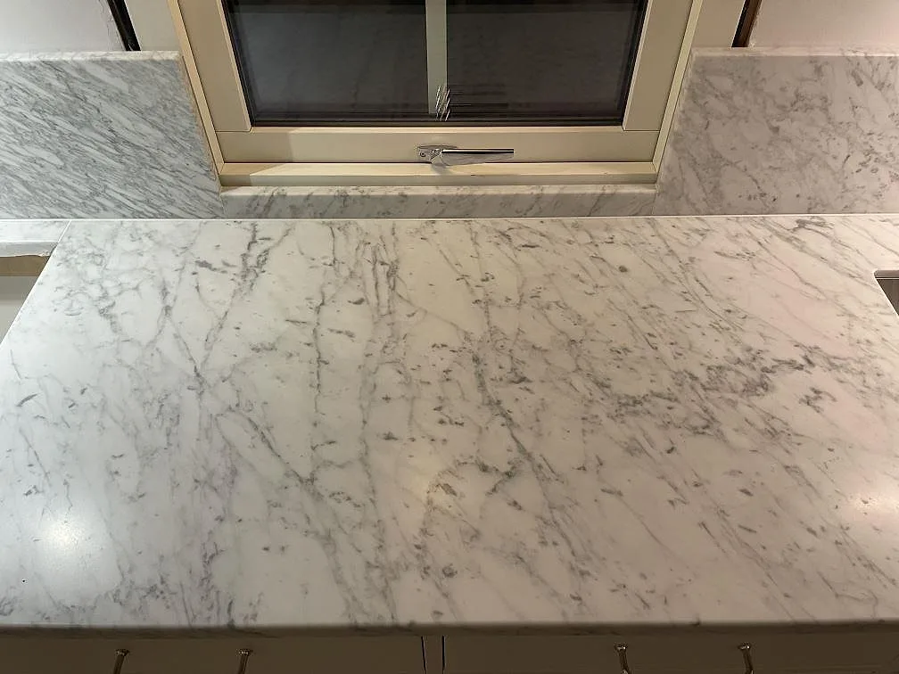 Närbild på matt Carrara C-marmor som köksbänkskiva framför fönster med stänkskydd och grå ådring i Avesta.