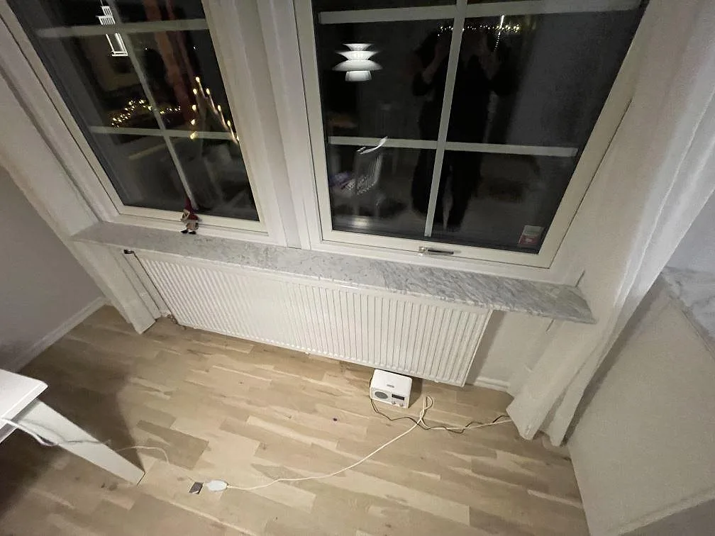 Lång fönsterbänk i matt Carrara C-marmor över radiator, monterad under två fönster i köket i Avesta.