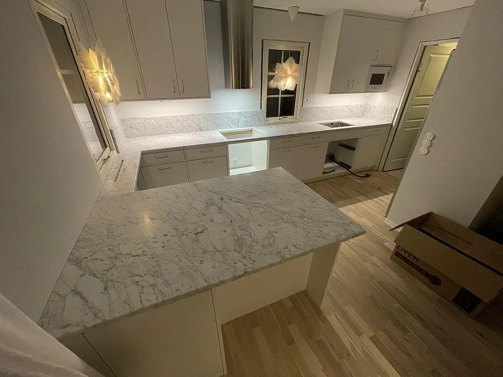 Köksbänkskiva och köksö i matt Carrara C-marmor med uppvikt stänkskydd i ett kök i Avesta.