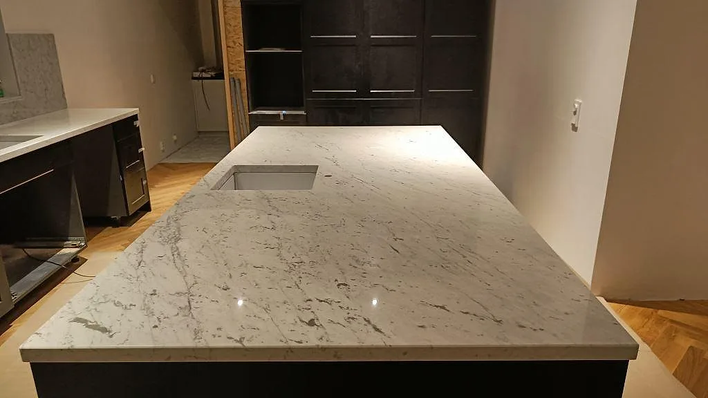 Köksbänkskiva och köksö i vit Carrara C marmor med grå ådring, polerad, med underlimmad rostfri diskho i ett kök i Bara.