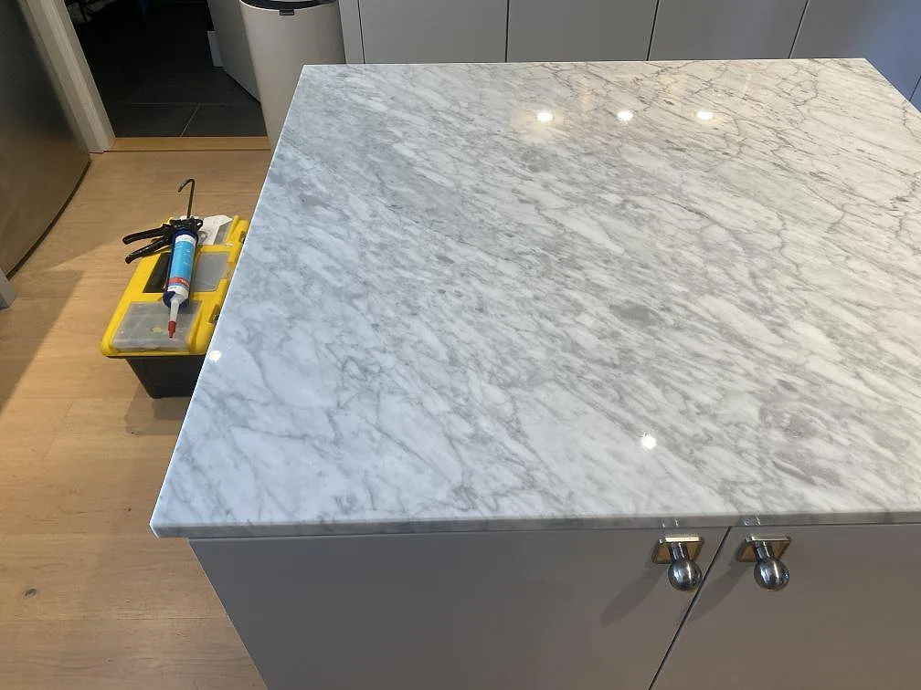 Närbild av polerad Carrara C marmor på köksö i Bara, med grå ådring och synlig stenprofil.