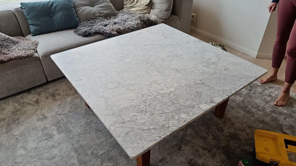 Bordsskiva i Carrara C-marmor, matt finish, med distinkt grå ådring, monterad på träben i ett vardagsrum i Billdal.