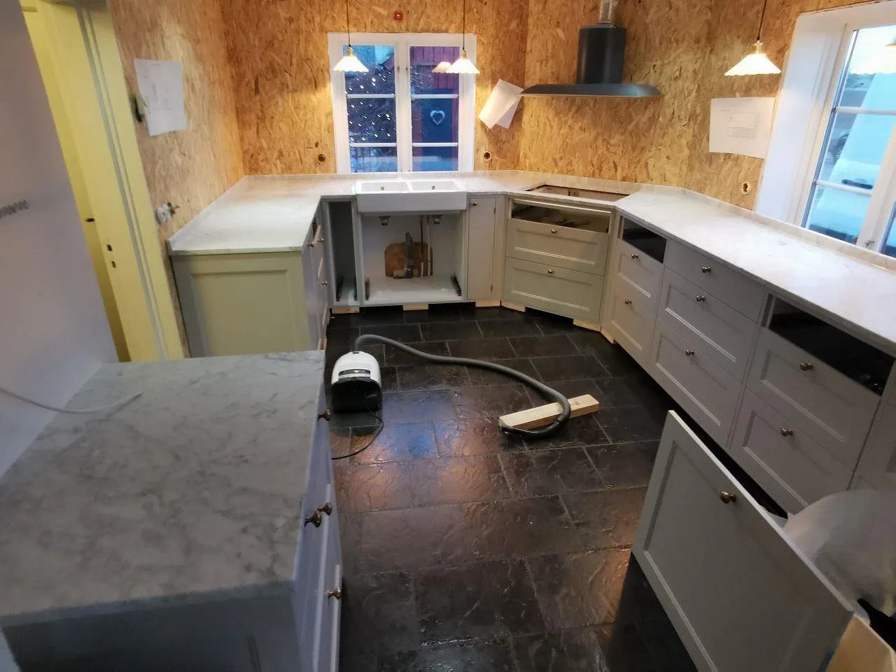 Köksbänkskiva i vit Carrara C-marmor med grå ådring, matt yta, monterad i ett kök under installation i Billeberga.