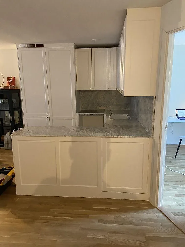 Kök i Borås med 20 mm polerad Carrara C marmor på bänk och stänkskydd mellan vita skåp.