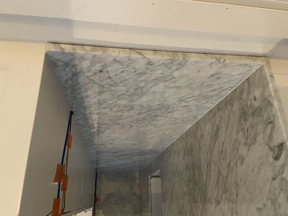 Närbild på stående väggbeklädnad i polerad Carrara C marmor under montering i Borås.