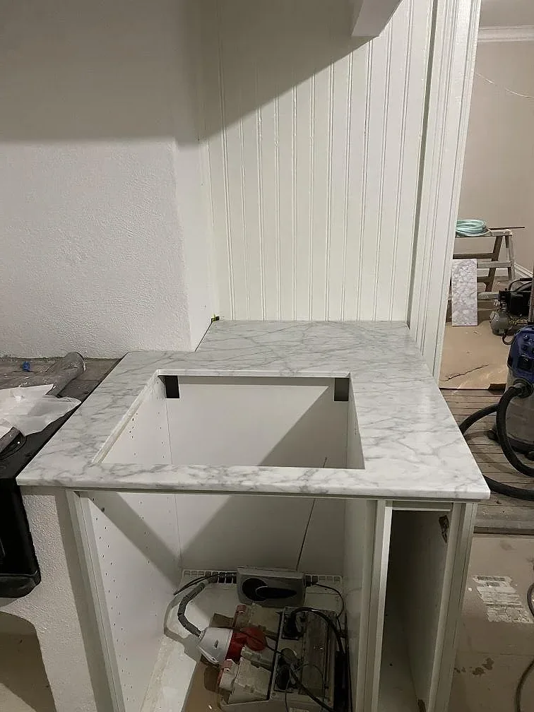 Matt köksbänkskiva och sidoklädd köksödel i Carrara C-marmor under montering i ett kök i Borås, med öppna stommar och synlig el bakom.