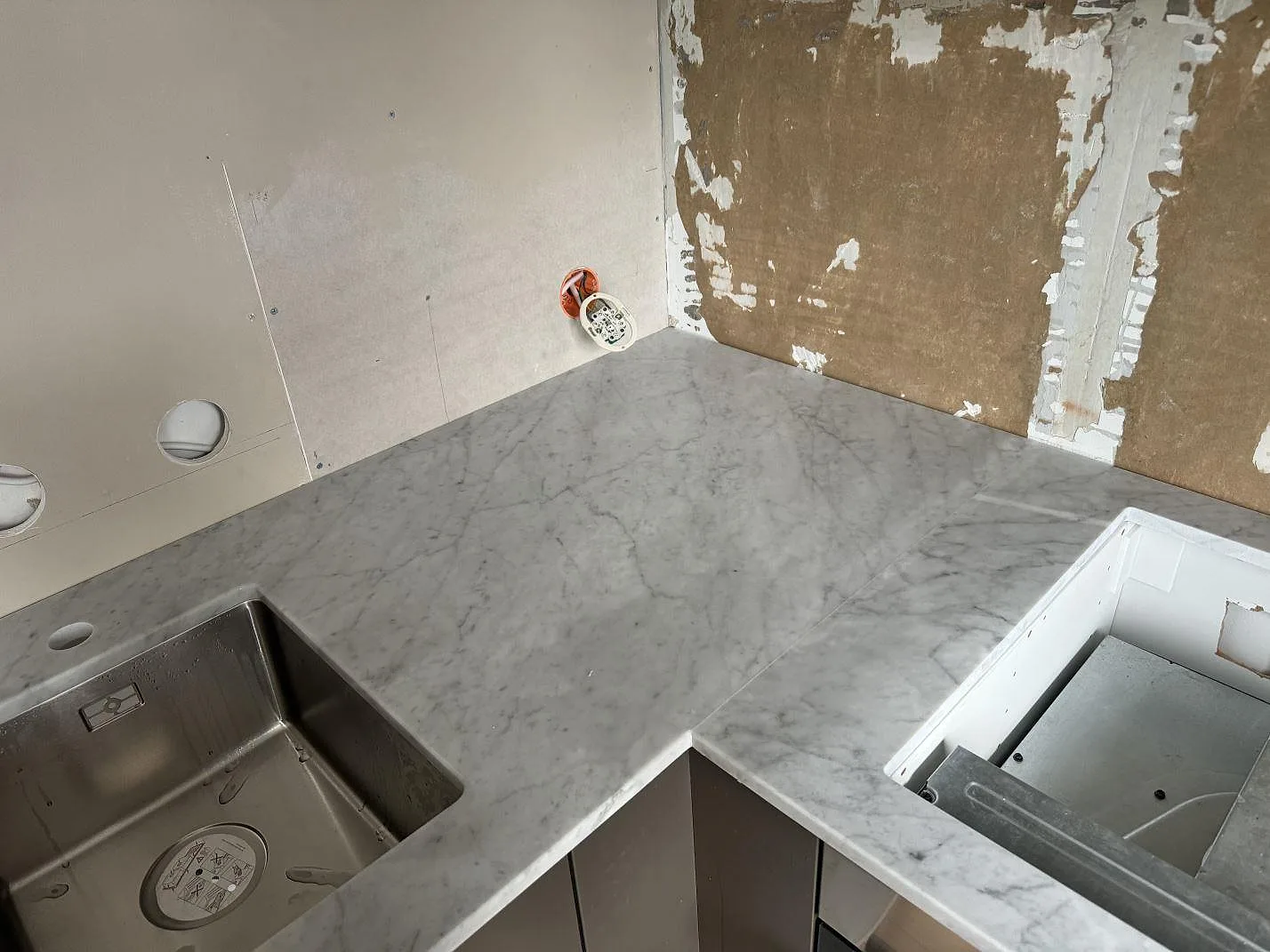 Hörn i kök i Borås med matt Carrara C marmor, rostfri diskho och urtag för häll i den L-formade bänkskivan.