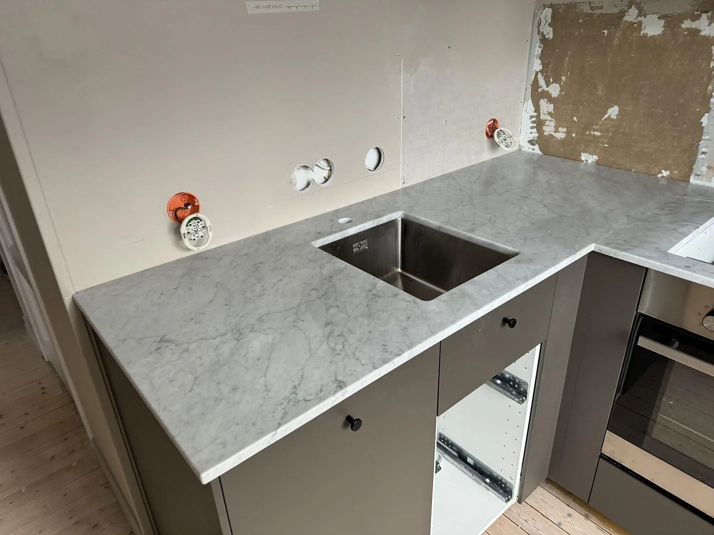 Matt Carrara C marmorbänkskiva i ett kök i Borås, med rostfri ho, urtag för häll och öppna lådstommar under montering.