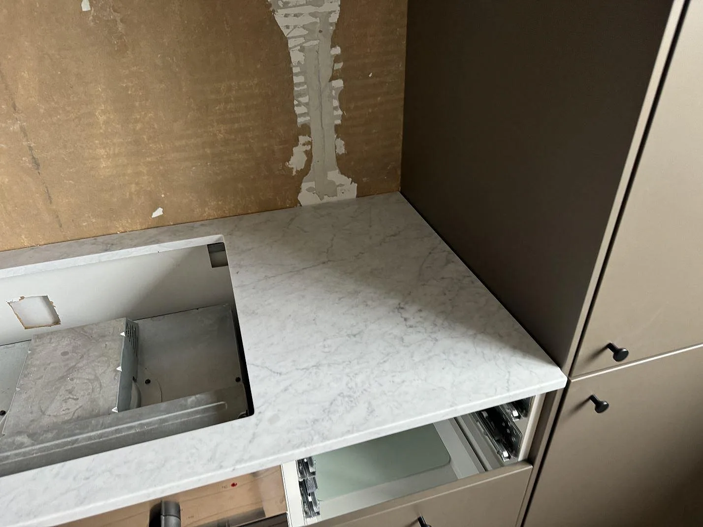Detalj av matt Carrara C marmorbänkskiva i Borås med hällurtag och grå ådring intill höga köksskåp.