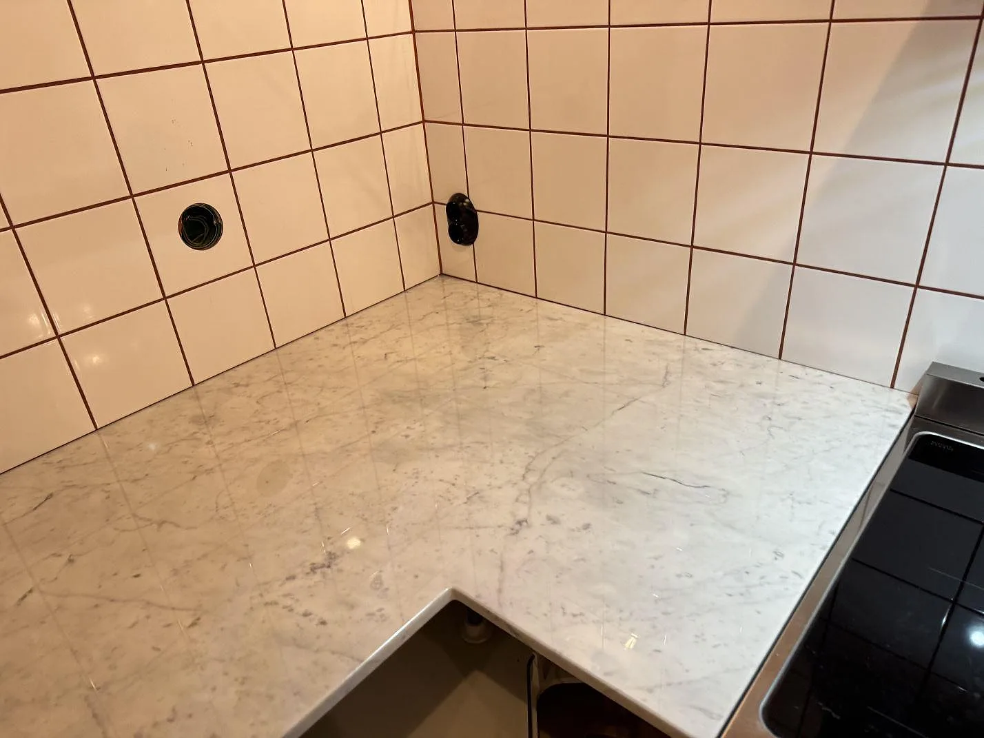 Polerad Carrara C-marmor som L-formad köksbänkskiva mot vitt kakel och spis i ett kök i Borrby.