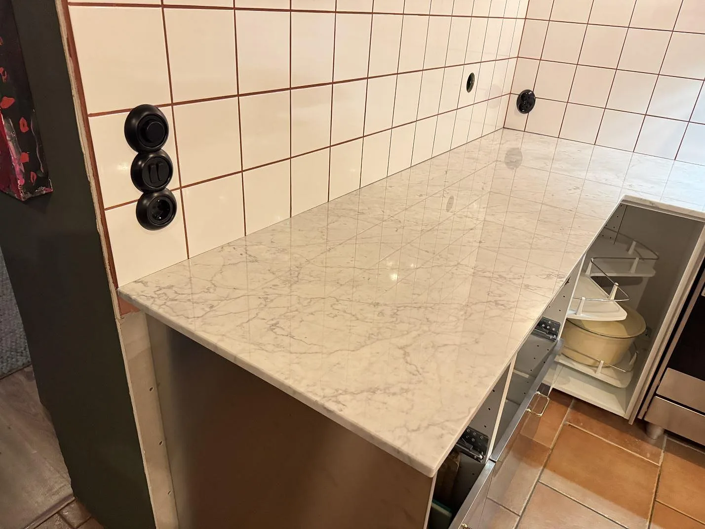 Polerad köksbänkskiva i Carrara C-marmor med grå ådring längs vit kakelvägg i ett kompakt kök i Borrby.