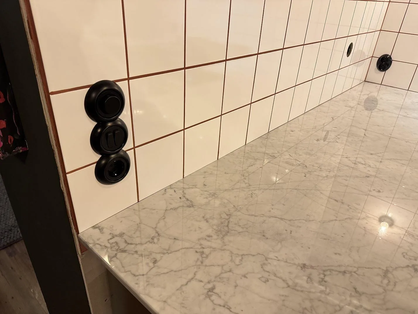 Detalj av polerad köksbänkskiva i Carrara C-marmor med vägguttag och vit kakelvägg i ett kök i Borrby.