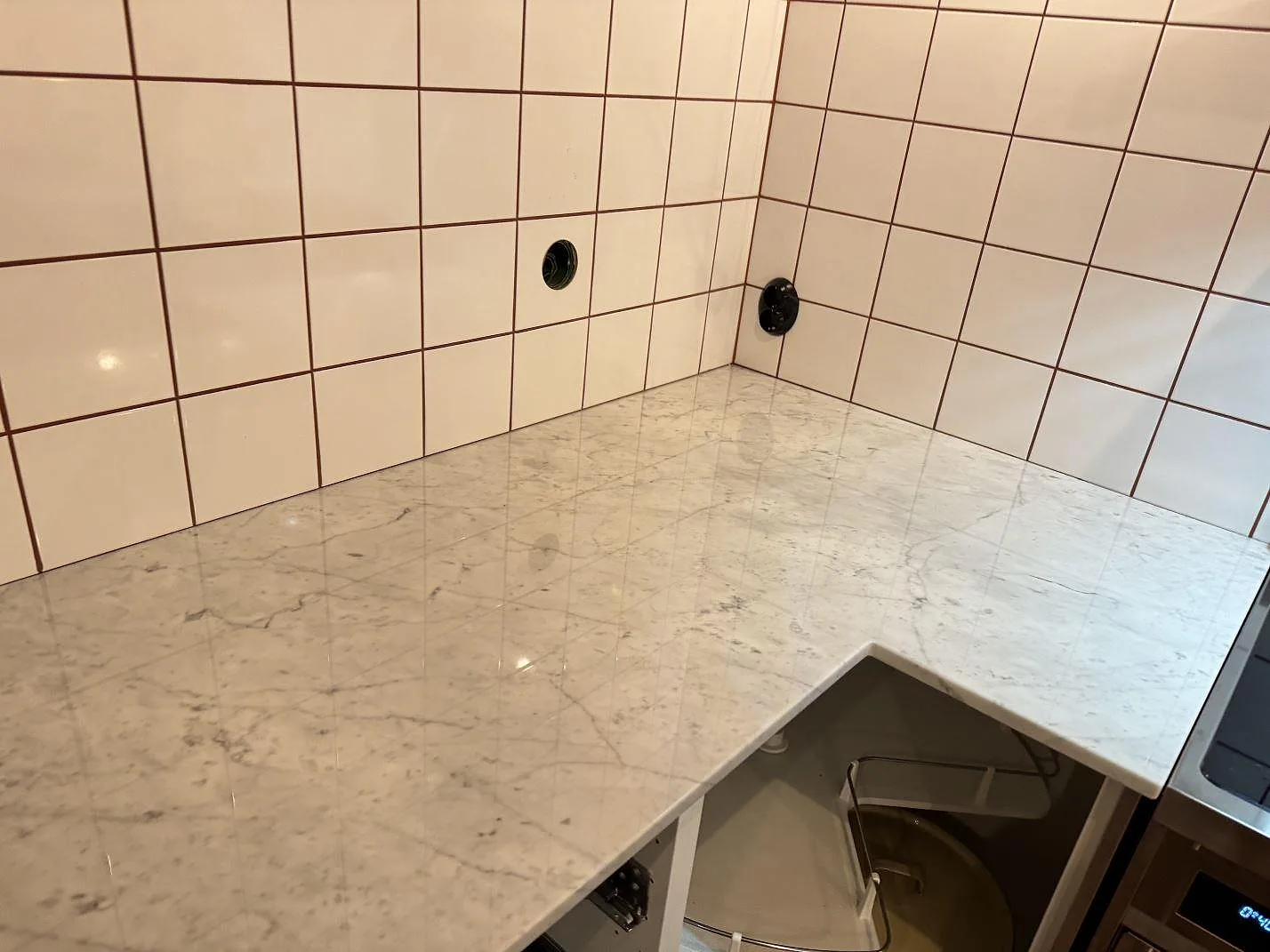 Närbild av polerad köksbänkskiva i Carrara C-marmor med hörnpassning och diskbänksdel i Borrby.