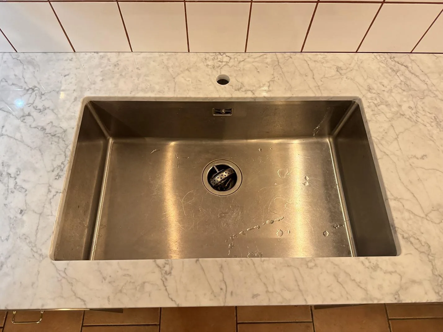 Rostfri diskho i en polerad köksbänkskiva av Carrara C-marmor, sedd ovanifrån i Borrby.