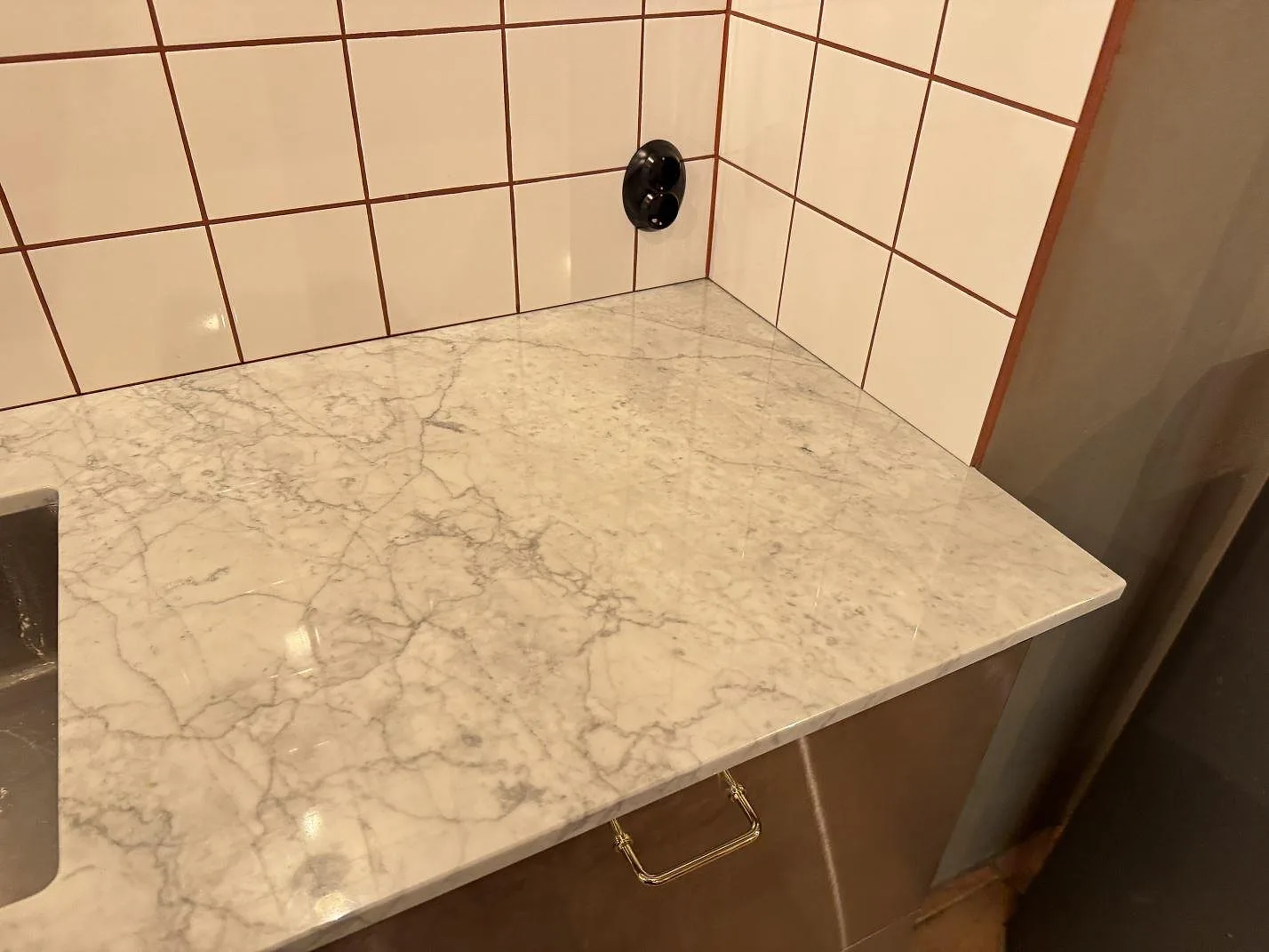 Polerad Carrara C-marmor som köksbänkskiva med tydlig grå ådring vid kaklad vägg i Borrby.