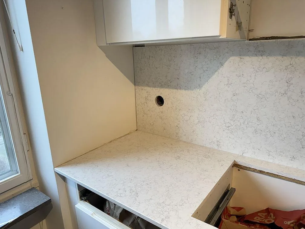 Köksbänkskiva i Carrara C-marmor, polerad, vid fönster med uppvikt marmorskiva på väggen i ett kök i Borrby.
