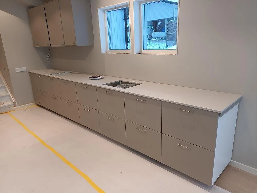 Lång köksbänkskiva i polerad Carrara C marmor, 20 mm, med öppningar för diskho och häll i ett kök under montering i Boxholm.