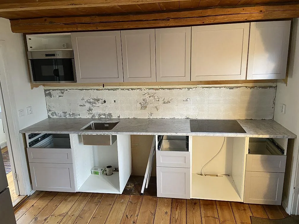 Köksbänkskiva i vit Carrara C-marmor med grå ådring, monterad i en rak köksrad med underlimmad diskho och infälld induktionshäll under montering i ett kök i Brantevik.