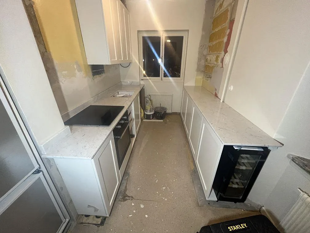Köksbänkskiva i Carrara C marmor, polerad 20 mm, med induktionshäll i ett smalt vitt kök i Bromma under montering.